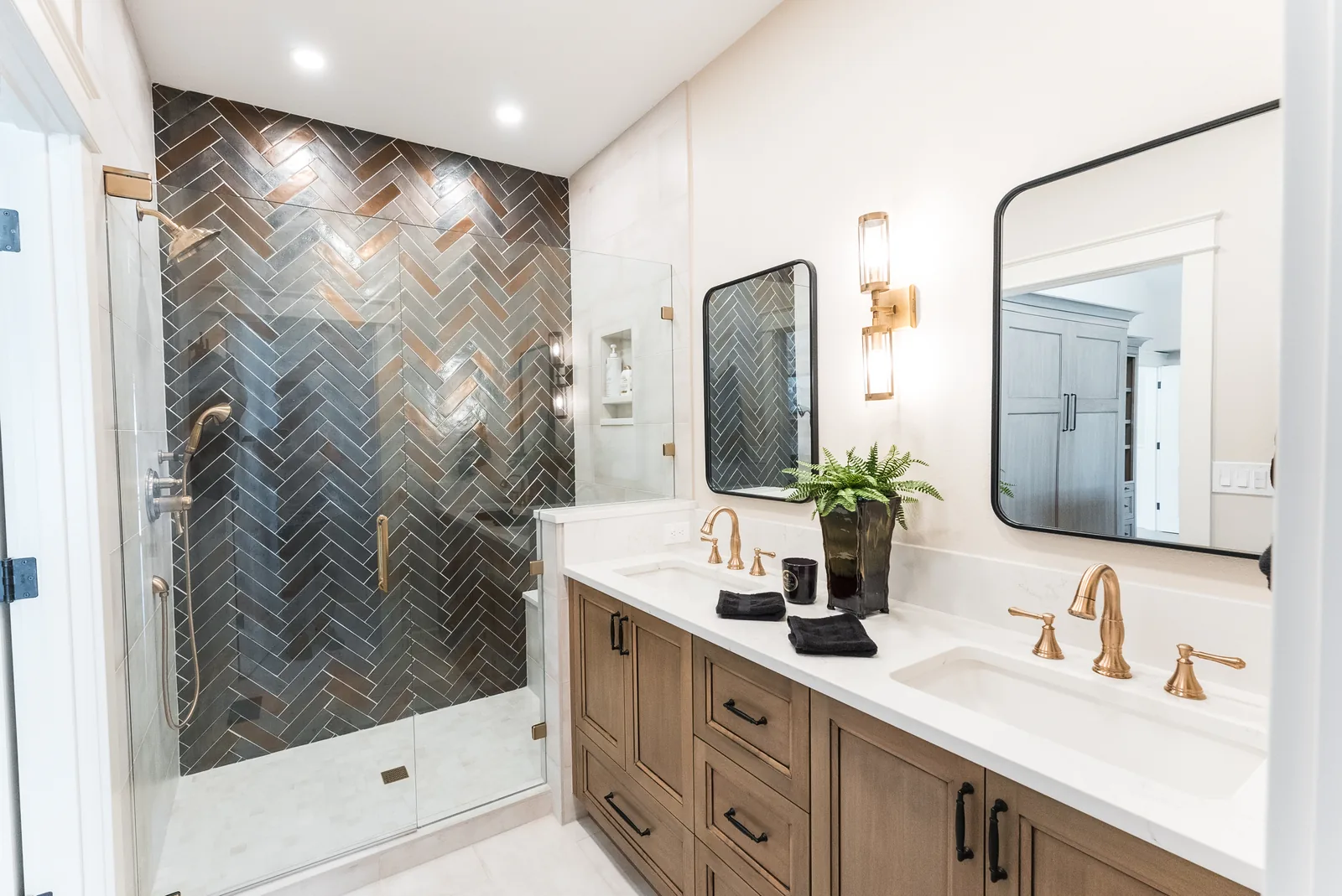 Primary bathroom with herringbone tile and brass sconce lighting installation